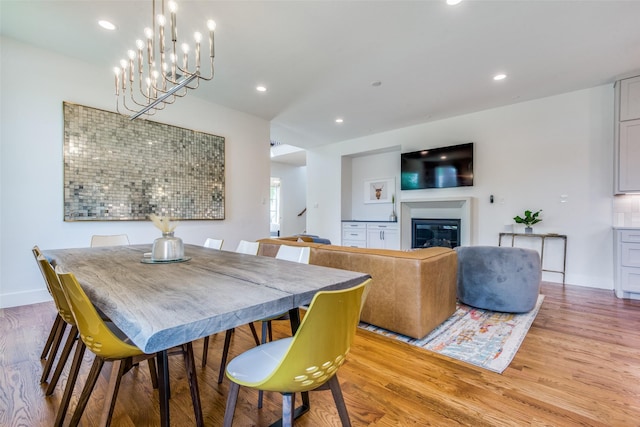 dining room featuring baseboards, light wood finished floors, a glass covered fireplace, and recessed lighting