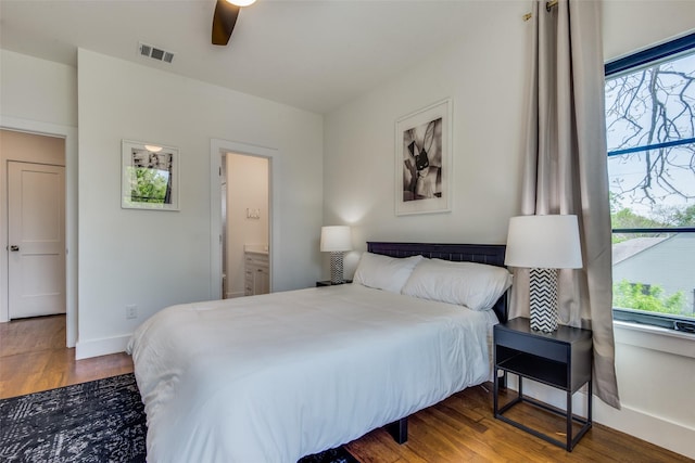 bedroom featuring baseboards, visible vents, ensuite bath, ceiling fan, and wood finished floors