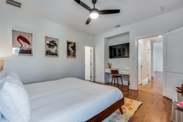 bedroom featuring built in desk, attic access, visible vents, and wood finished floors