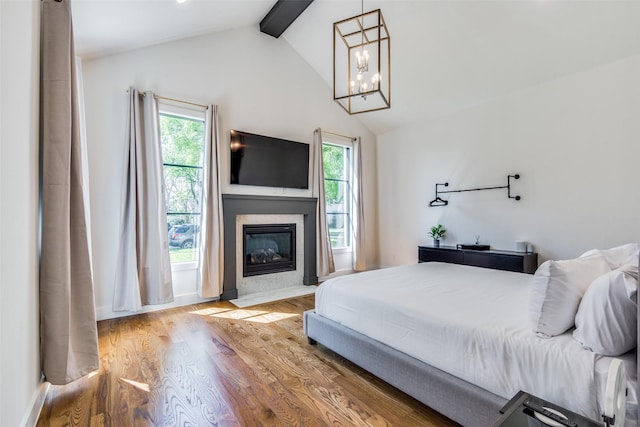 bedroom featuring a fireplace with flush hearth, lofted ceiling with beams, an inviting chandelier, and wood finished floors