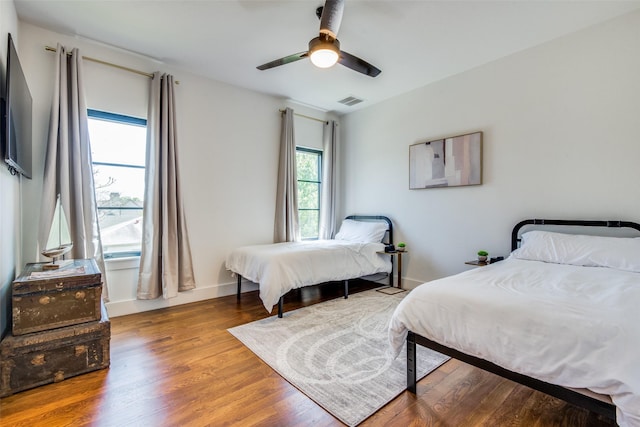 bedroom with a ceiling fan, wood finished floors, visible vents, and baseboards