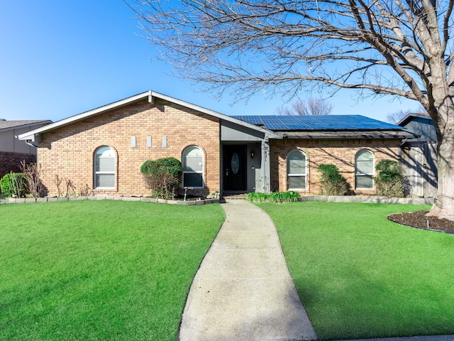 single story home with brick siding, a front lawn, and roof mounted solar panels