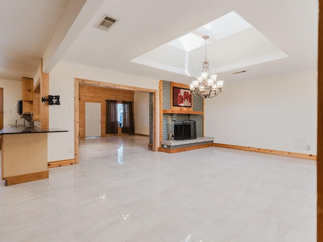 unfurnished living room with a skylight, a raised ceiling, visible vents, a brick fireplace, and baseboards