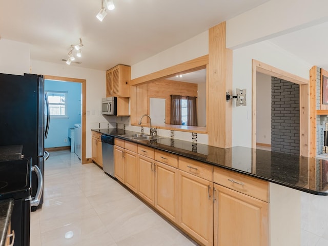 kitchen with a sink, appliances with stainless steel finishes, decorative backsplash, dark stone counters, and light brown cabinetry