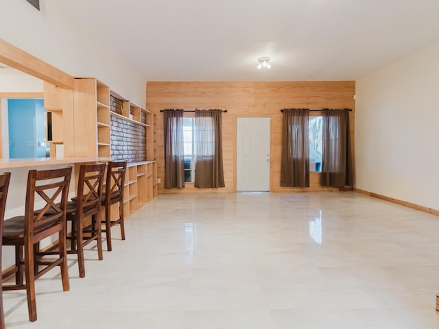 interior space featuring a breakfast bar, open shelves, light brown cabinetry, wood walls, and baseboards