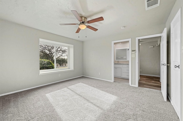 unfurnished bedroom with baseboards, visible vents, connected bathroom, light colored carpet, and ceiling fan