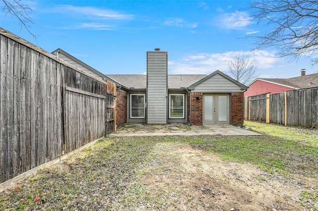 rear view of property featuring a patio, brick siding, a chimney, and a fenced backyard