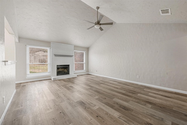 unfurnished living room with wood finished floors, visible vents, a ceiling fan, vaulted ceiling, and a brick fireplace