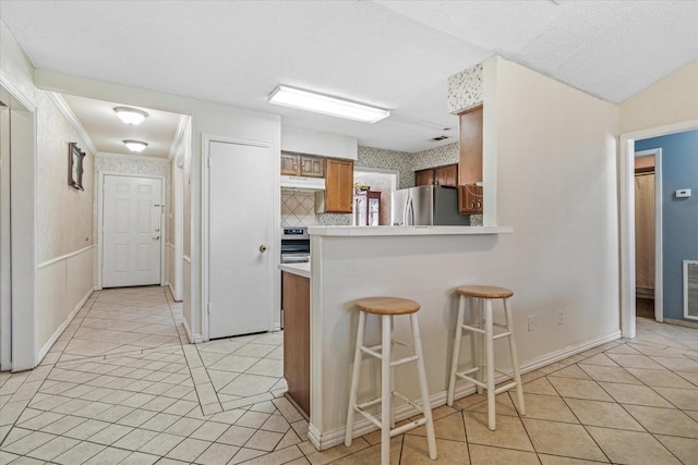 kitchen featuring under cabinet range hood, appliances with stainless steel finishes, brown cabinets, and light tile patterned flooring