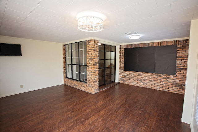 empty room featuring brick wall, wood finished floors, visible vents, and baseboards