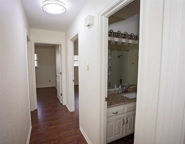 hallway with dark wood-type flooring, a sink, and baseboards