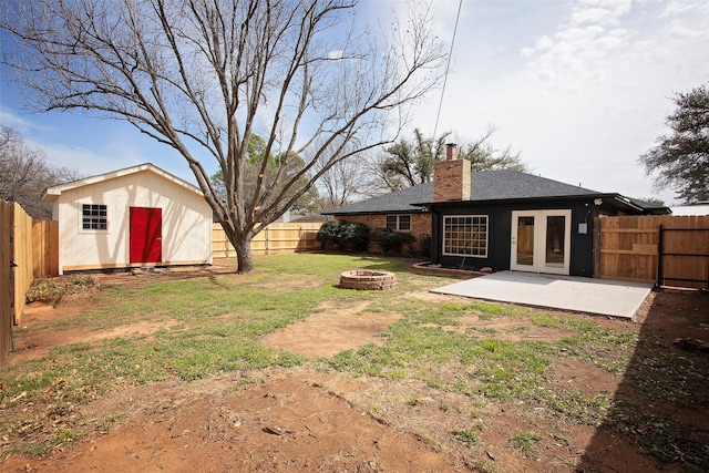 view of yard featuring french doors, a patio, a fenced backyard, an outdoor structure, and a fire pit