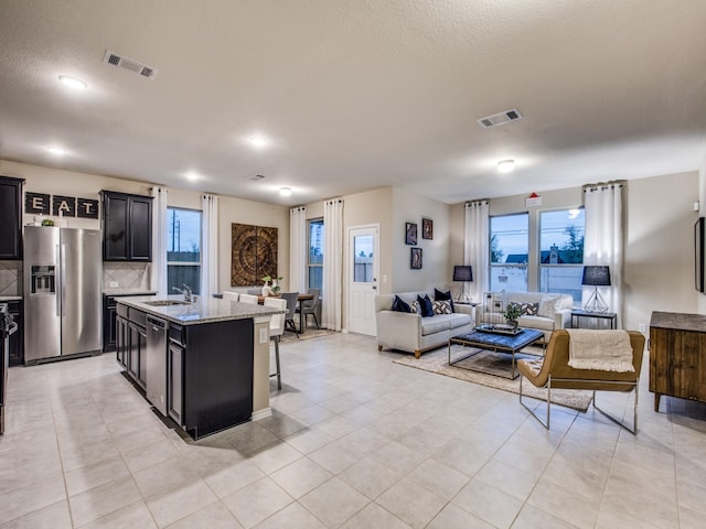 kitchen featuring stainless steel appliances, visible vents, open floor plan, a sink, and an island with sink