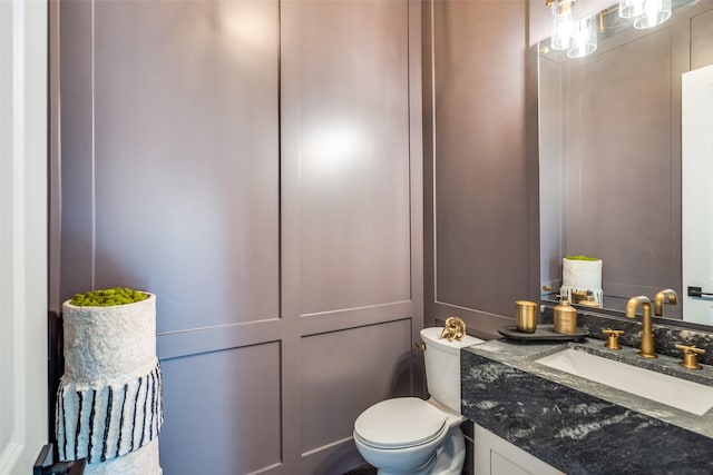 half bathroom with vanity, toilet, and a decorative wall