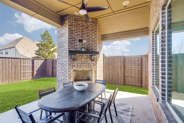 view of patio / terrace with an outdoor brick fireplace, outdoor dining area, a fenced backyard, and a ceiling fan