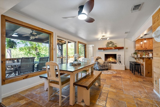 dining space with stone tile floors, a fireplace, a ceiling fan, baseboards, and visible vents