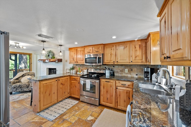 kitchen featuring stone tile floors, visible vents, appliances with stainless steel finishes, a peninsula, and a sink