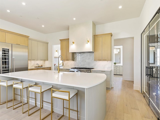 kitchen featuring light wood-style flooring, a sink, backsplash, a spacious island, and range