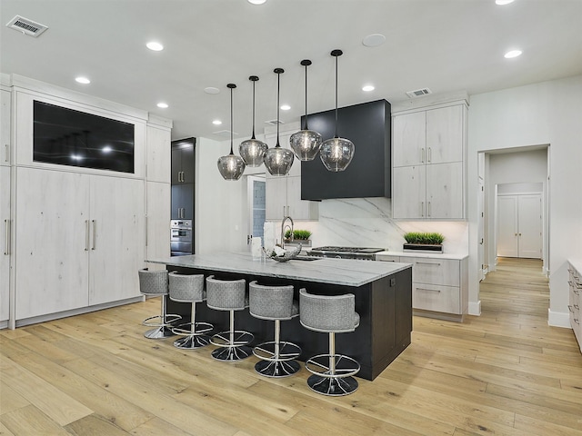 kitchen featuring range hood, light wood-style flooring, visible vents, and a sink