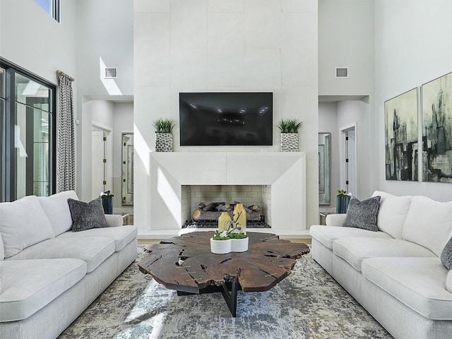 living area with visible vents, a fireplace, a towering ceiling, and wood finished floors