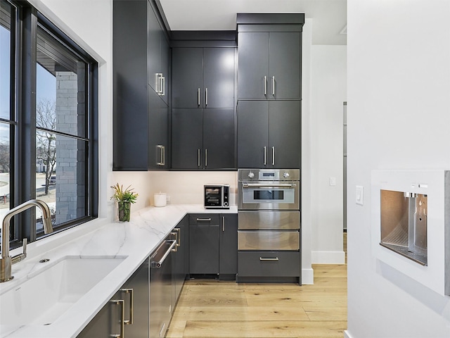 kitchen with a warming drawer, a sink, light stone counters, stainless steel appliances, and light wood-style floors