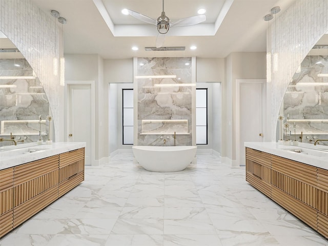 full bathroom with marble finish floor, a sink, a tray ceiling, recessed lighting, and a soaking tub