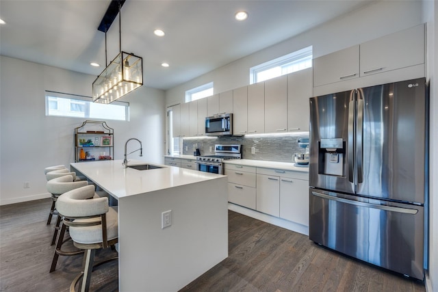 kitchen featuring dark wood finished floors, decorative backsplash, appliances with stainless steel finishes, light countertops, and a sink