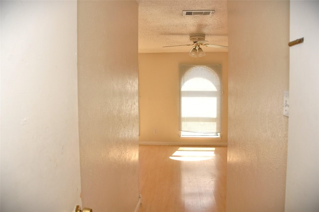 hall with a textured ceiling, wood finished floors, and visible vents