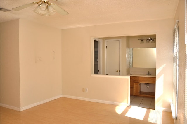 spare room with light wood finished floors, visible vents, baseboards, a ceiling fan, and a textured ceiling