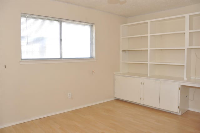 spare room featuring light wood-style floors, a textured ceiling, baseboards, and a ceiling fan