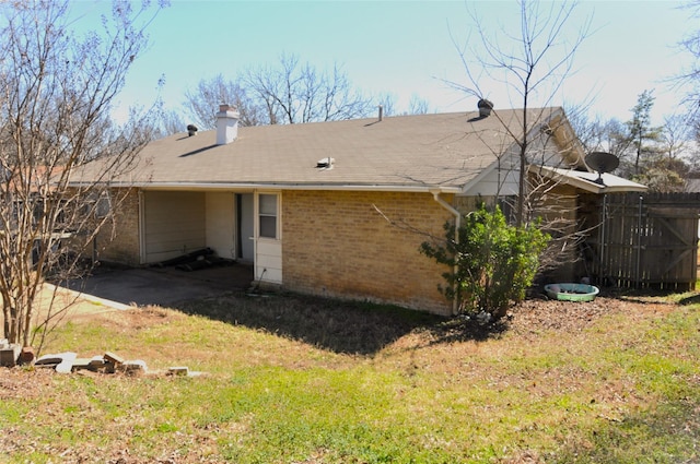 rear view of property featuring brick siding, a yard, a chimney, and fence