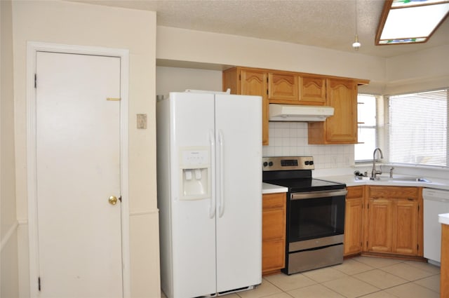 kitchen with white appliances, decorative backsplash, light countertops, under cabinet range hood, and a sink