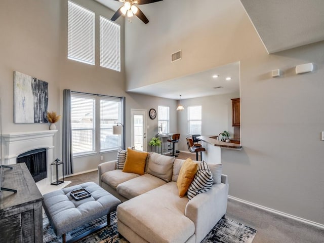 living room featuring visible vents, baseboards, a fireplace, ceiling fan, and light colored carpet