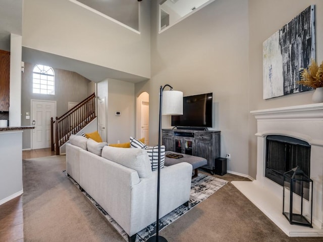 living area with a fireplace with raised hearth, stairway, arched walkways, a high ceiling, and carpet flooring