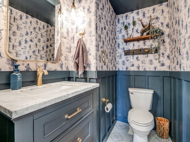 bathroom featuring vanity, a wainscoted wall, wallpapered walls, tile patterned flooring, and toilet