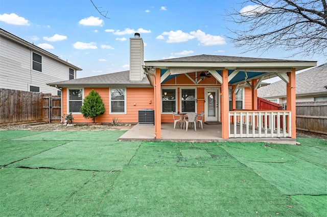 back of property with a patio, roof with shingles, central AC unit, fence private yard, and a chimney