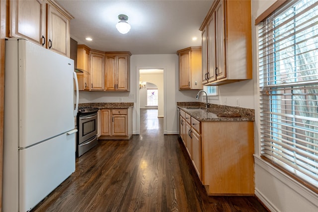 kitchen featuring arched walkways, stainless steel range, freestanding refrigerator, a sink, and dark stone counters