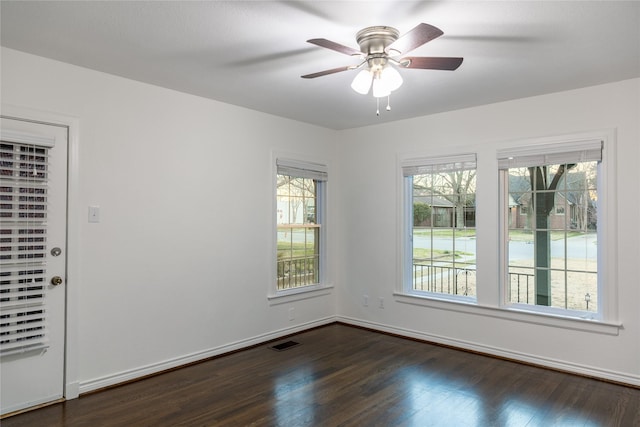 spare room featuring dark wood-type flooring, plenty of natural light, visible vents, and baseboards