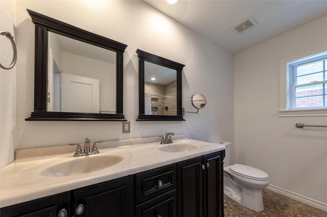 bathroom with toilet, double vanity, visible vents, and a sink