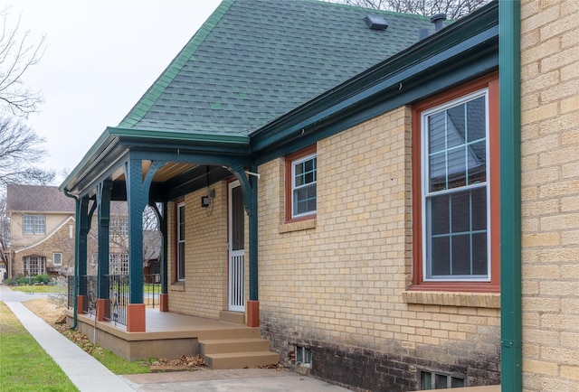 exterior space featuring covered porch, brick siding, and roof with shingles