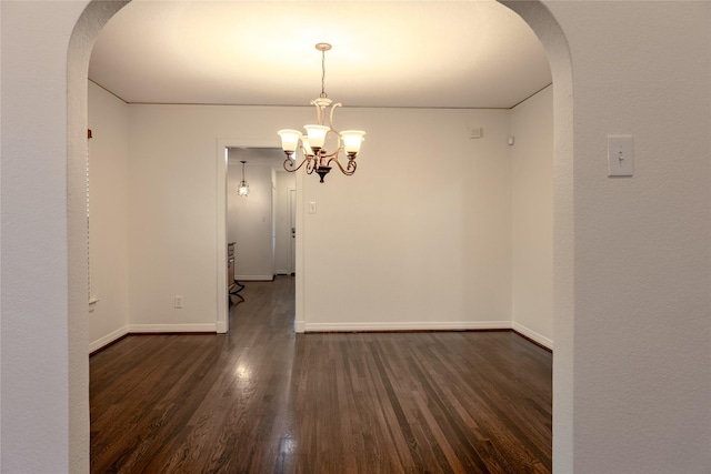 unfurnished dining area featuring arched walkways, dark wood-style flooring, and baseboards