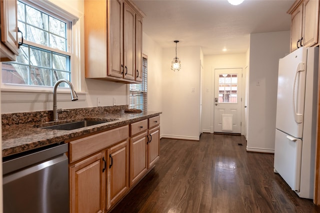 kitchen featuring dark wood-style flooring, stainless steel dishwasher, freestanding refrigerator, a sink, and dark stone counters