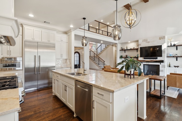 kitchen featuring a large fireplace, white cabinets, dark wood-style floors, stainless steel appliances, and a sink