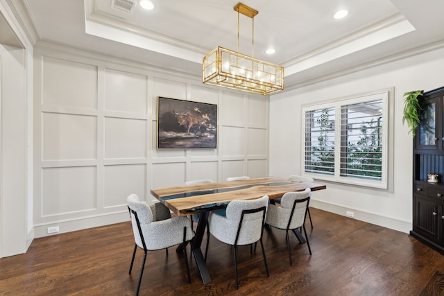 dining area with visible vents, ornamental molding, dark wood-style flooring, a tray ceiling, and a decorative wall