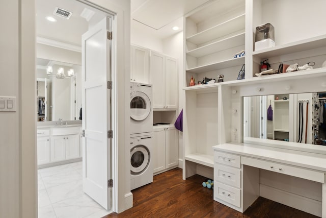 laundry room with cabinet space, stacked washer and dryer, visible vents, marble finish floor, and a sink