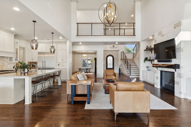 living area featuring a fireplace, stairway, a towering ceiling, dark wood-type flooring, and a chandelier