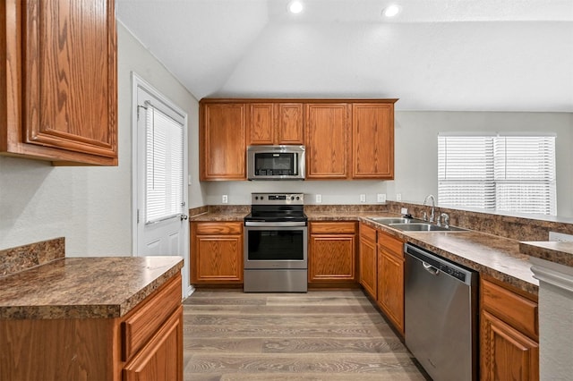 kitchen featuring appliances with stainless steel finishes, dark countertops, a sink, and light wood-style flooring