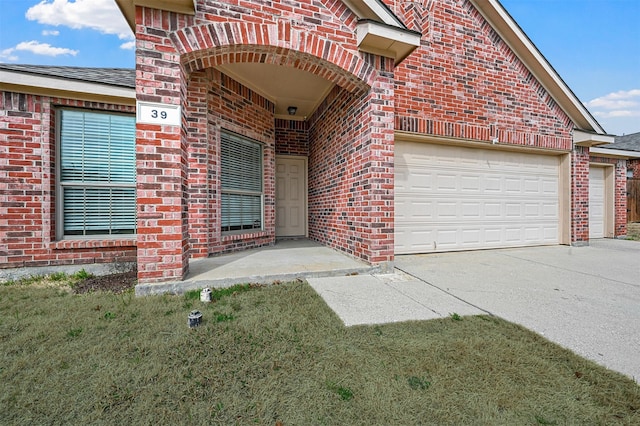 entrance to property with brick siding, driveway, an attached garage, and roof with shingles