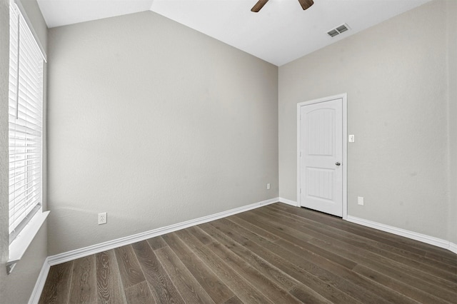 empty room featuring lofted ceiling, dark wood-style flooring, visible vents, baseboards, and a ceiling fan