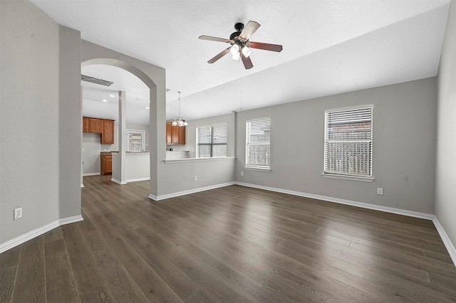 unfurnished living room featuring arched walkways, ceiling fan with notable chandelier, visible vents, baseboards, and dark wood finished floors